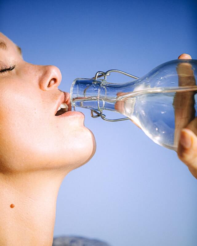 A woman drinking water from a glass bottle depicting proper hydration which is essential on starting keto diet